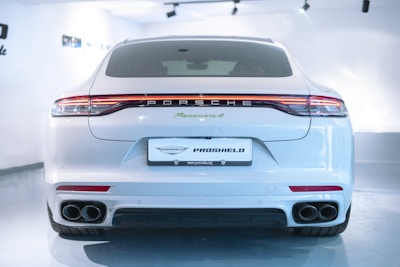 A sleek white sports car is parked indoors, showcasing its rear view with a prominent brand logo and twin exhausts. The vehicle is well-lit, highlighting its elegant curves and modern design.