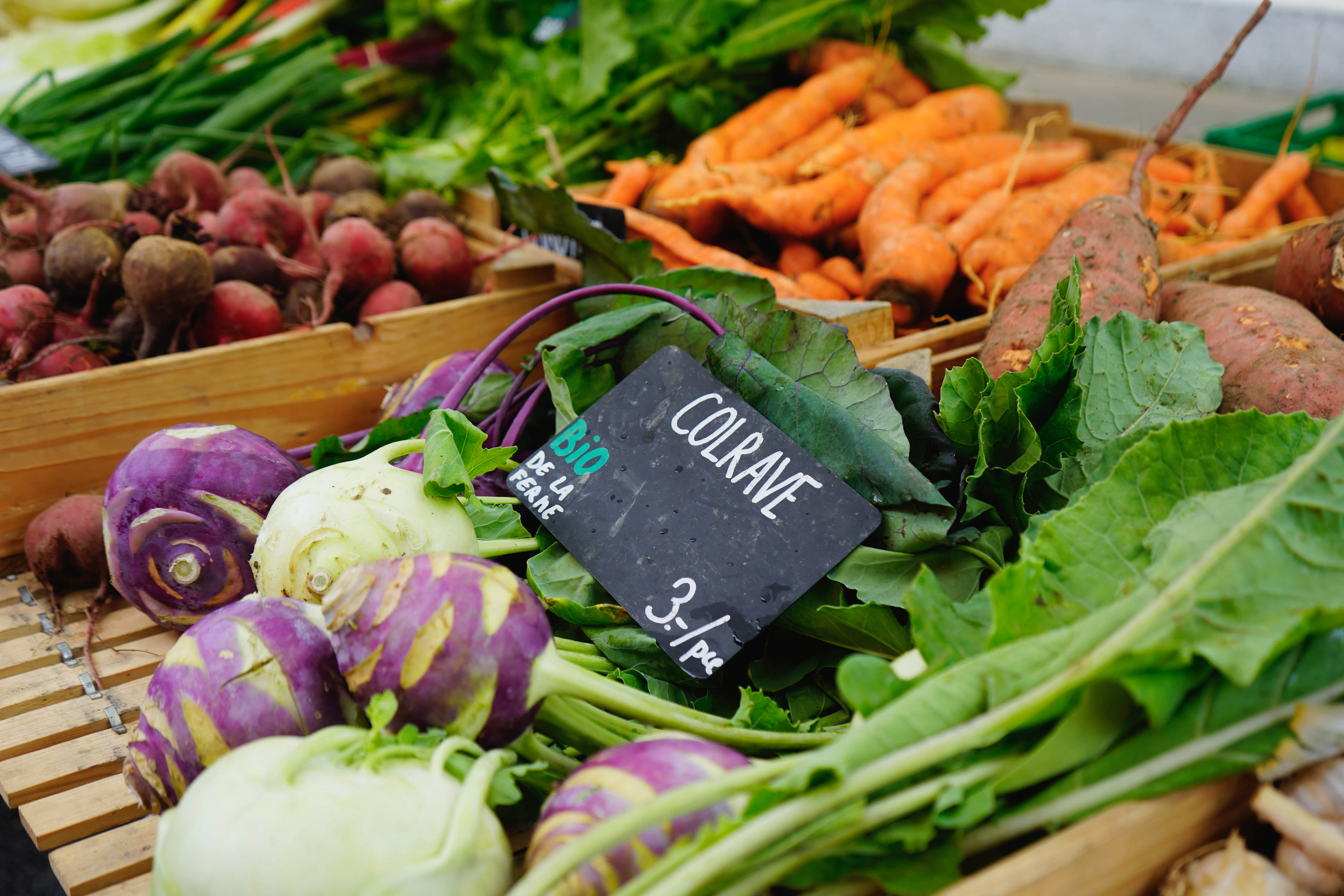 A market stall displays beets, carrots and kohlrabi beside a hand-chalked French price sign.