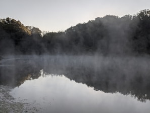 A calm lake reflecting the sky during early morning mist.