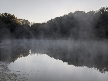 A calm lake reflecting the sky during early morning mist.