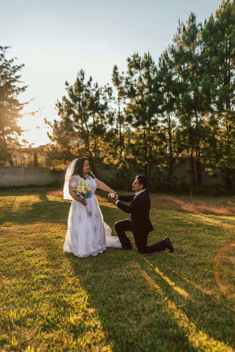 a man and woman in wedding attire sitting on grass with trees in the background