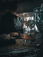 A collection of elegant glassware is placed on a table, featuring a mix of turquoise and clear glasses. The scene is dimly lit, creating reflections and shadows that enhance the luxurious feel. The table surface has a patterned design and holds additional items, including a small black object and a translucent bag.