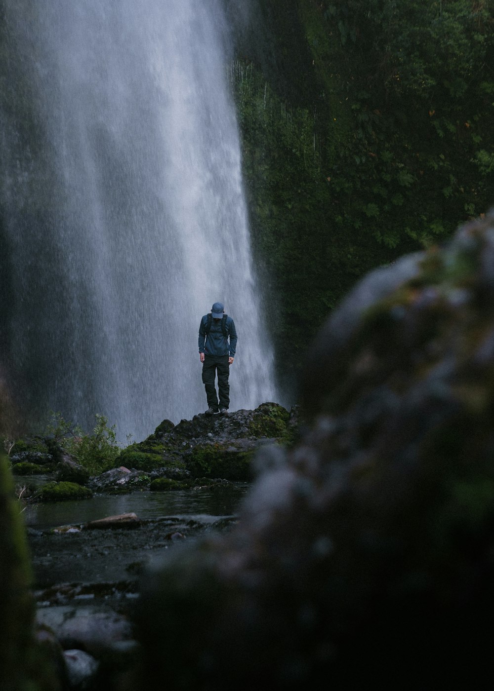 a person standing on a rock near a waterfall