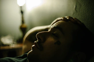 Person lying back in a dim room with a hand on the forehead, sleep stories for adults at bedtime