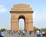 a large stone arch with people walking around with India Gate in the background