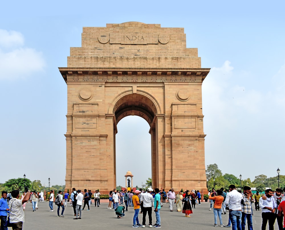 ein großer Steinbogen mit Menschen, die mit dem India Gate im Hintergrund herumlaufen