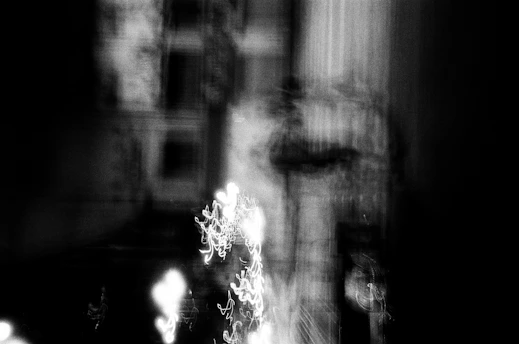 A surreal black and white photograph featuring abstract shapes blending into a shadowy urban landscape.