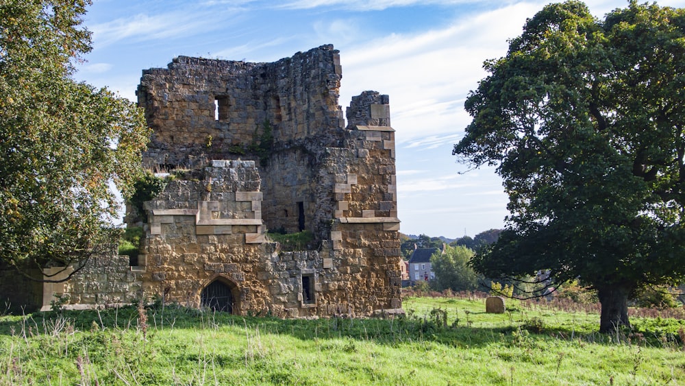 a stone building with a grass field with Ashby de la Zouch Castle in the background
