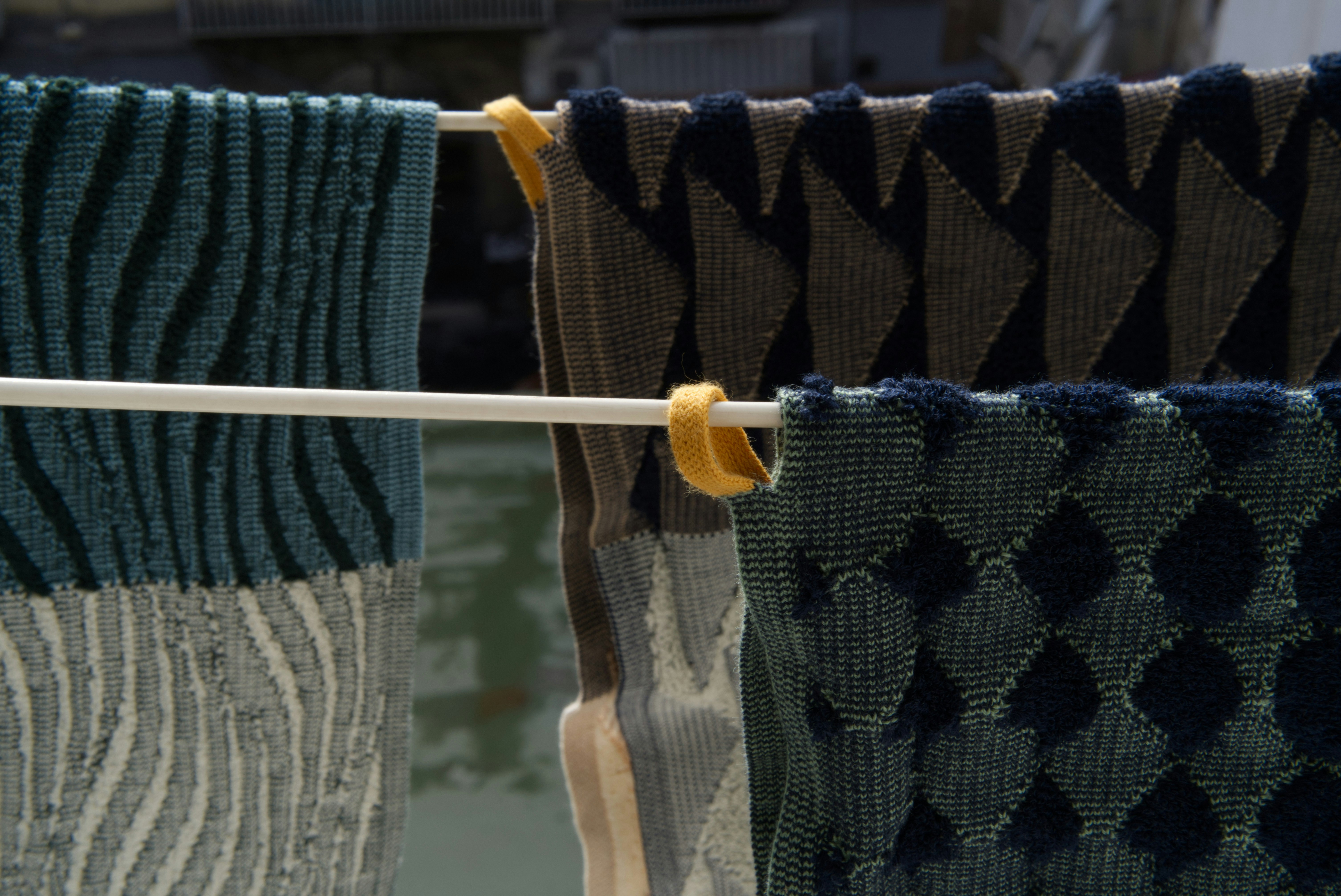 Three knitted towels hanging on lines in the sun. Made in Berlin by Towel.Studio, these towel feature alternating patterns of terry and standard knitted stitches.