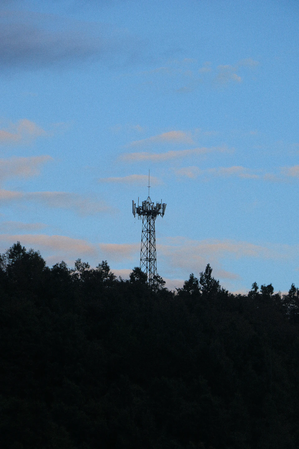 Tall gray cell tower standing against clear blue sky with surrounding lush green landscape