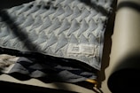 A folded textile piece made from 100% organic cotton with a geometric chevron pattern. The label, indicating it's from towel studio and made in Germany, is visible. The fabric appears to be draped on a flat surface, with one edge slightly in shadow.