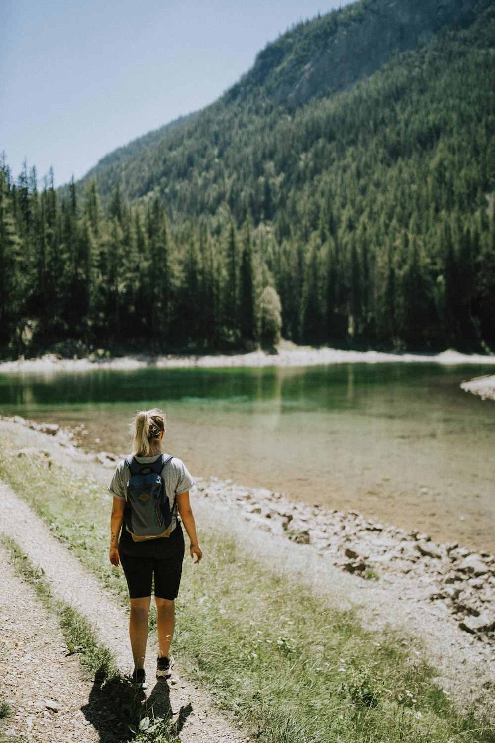 a man walking on a path by a lake with trees and mountains in the background