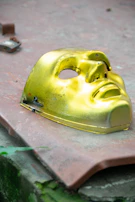 A minimalist gold mask resting on a dark glass surface, surrounded by subtle reflections and soft shadows.