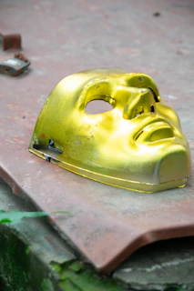 A minimalist gold mask resting on a dark glass surface, surrounded by subtle reflections and soft shadows.
