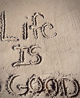 The words 'Life is Good' are written in the sand with visible texture and shadows.