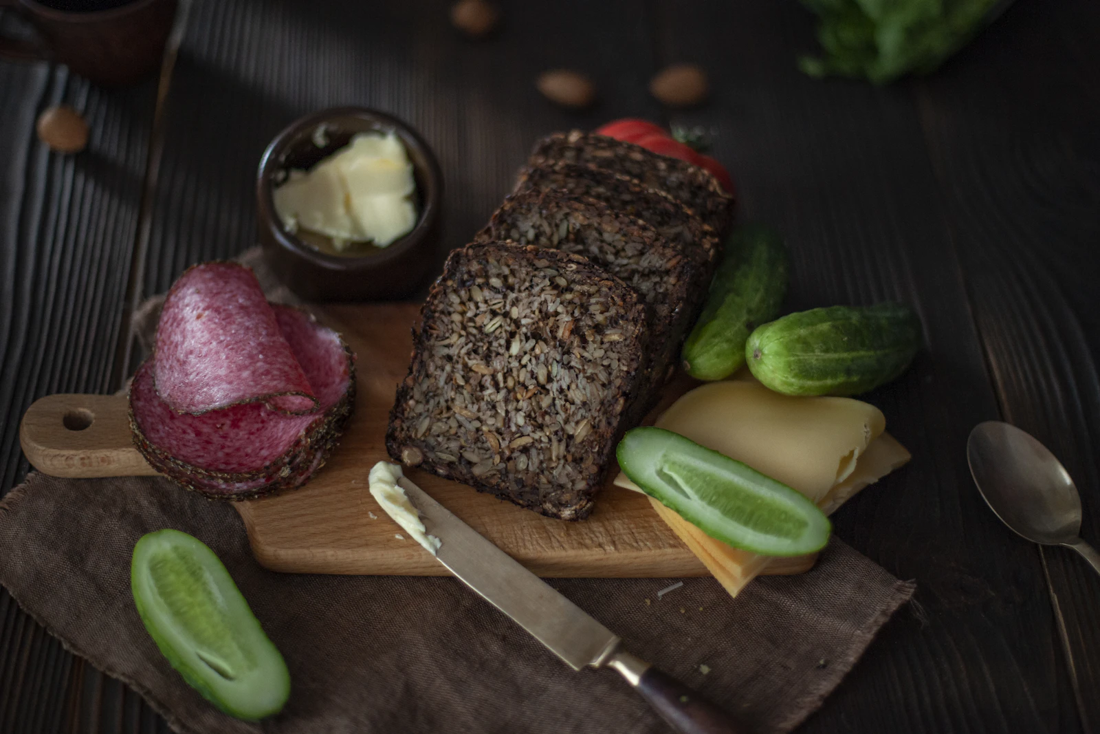 Sliced black rye on a board with butter, cucumbers and onion