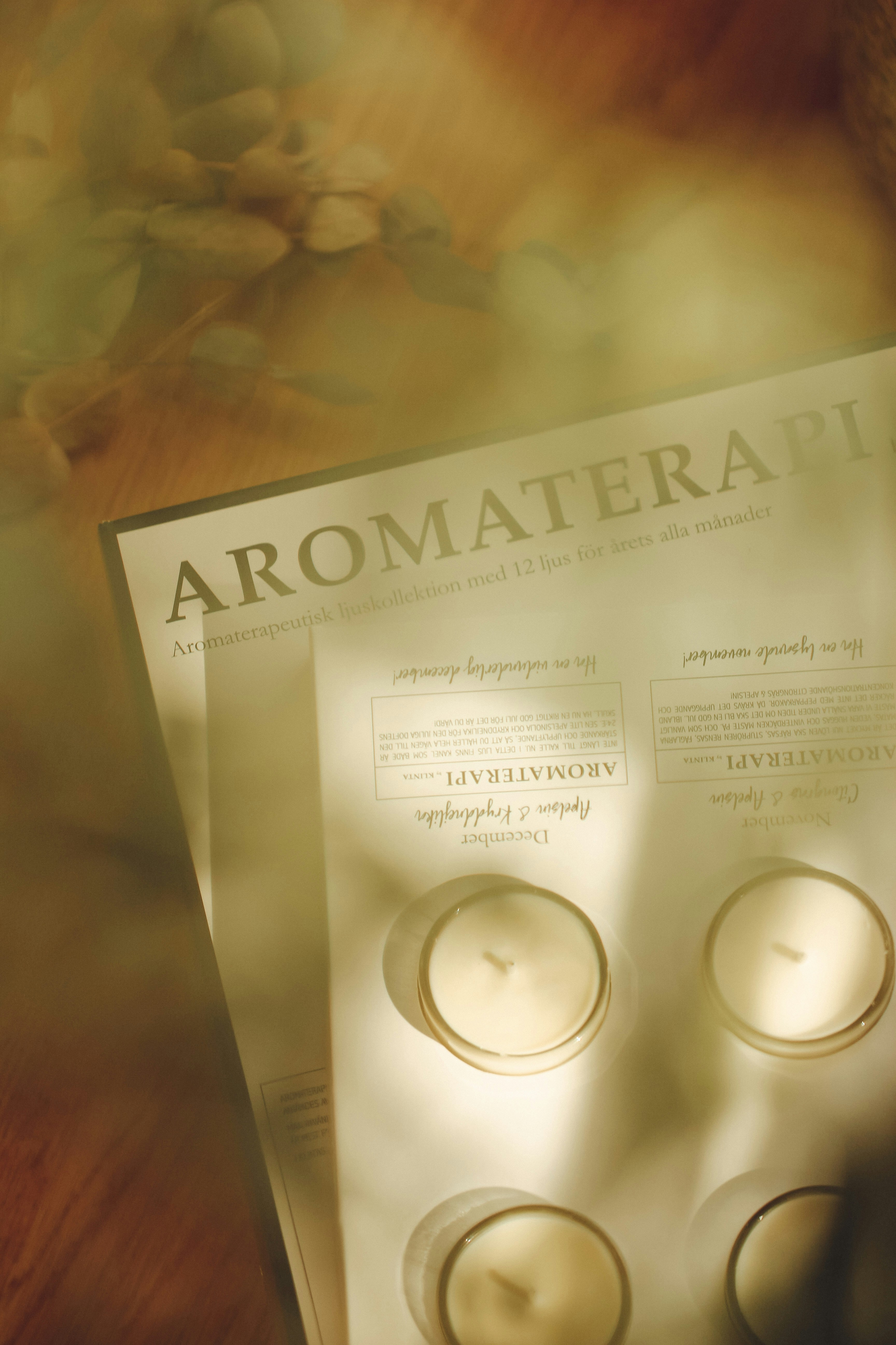 Broschyrsidor om aromaterapi bredvid fyra små vita ljus.