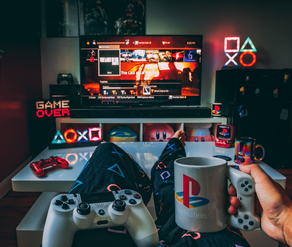a person holding a cup and a game controller in front of a television
