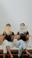 a man and woman sitting on a couch reading a book