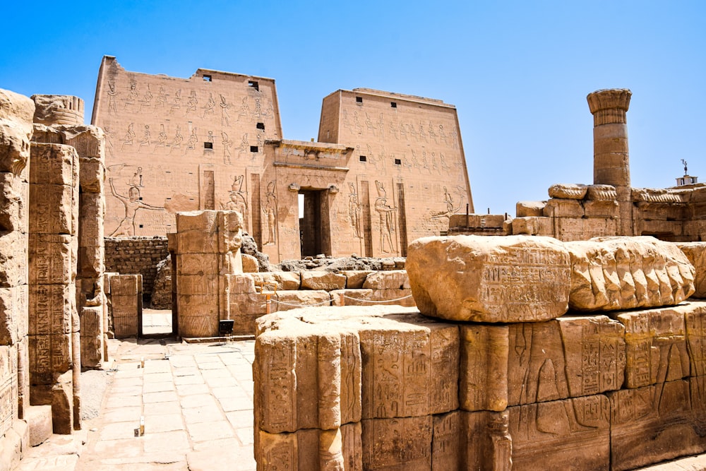 a group of stone buildings with Temple of Edfu in the background