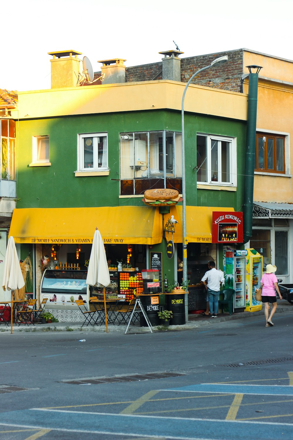 a yellow building with a green awning and a couple people walking by