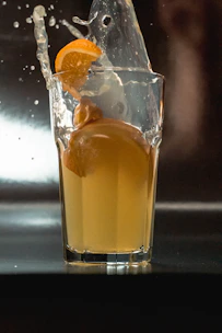 Close-up of vibrant fruit juices splashing into clear glasses on a bright background.