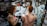 A tattoo artist is working on the back of a person with red hair, creating a large, intricate snake design. The studio has artistic wall decorations with black swirls and framed artwork. The artist has a detailed tattoo on their arm, and there is a mirror reflecting parts of the scene.