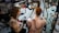 A tattoo artist is working on the back of a person with red hair, creating a large, intricate snake design. The studio has artistic wall decorations with black swirls and framed artwork. The artist has a detailed tattoo on their arm, and there is a mirror reflecting parts of the scene.