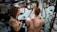 A tattoo artist is working on the back of a person with red hair, creating a large, intricate snake design. The studio has artistic wall decorations with black swirls and framed artwork. The artist has a detailed tattoo on their arm, and there is a mirror reflecting parts of the scene.