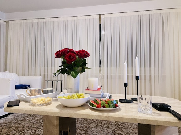 A cozy living room corner with velvet cushions, soft lighting, and a marble coffee table styled with fresh flowers.