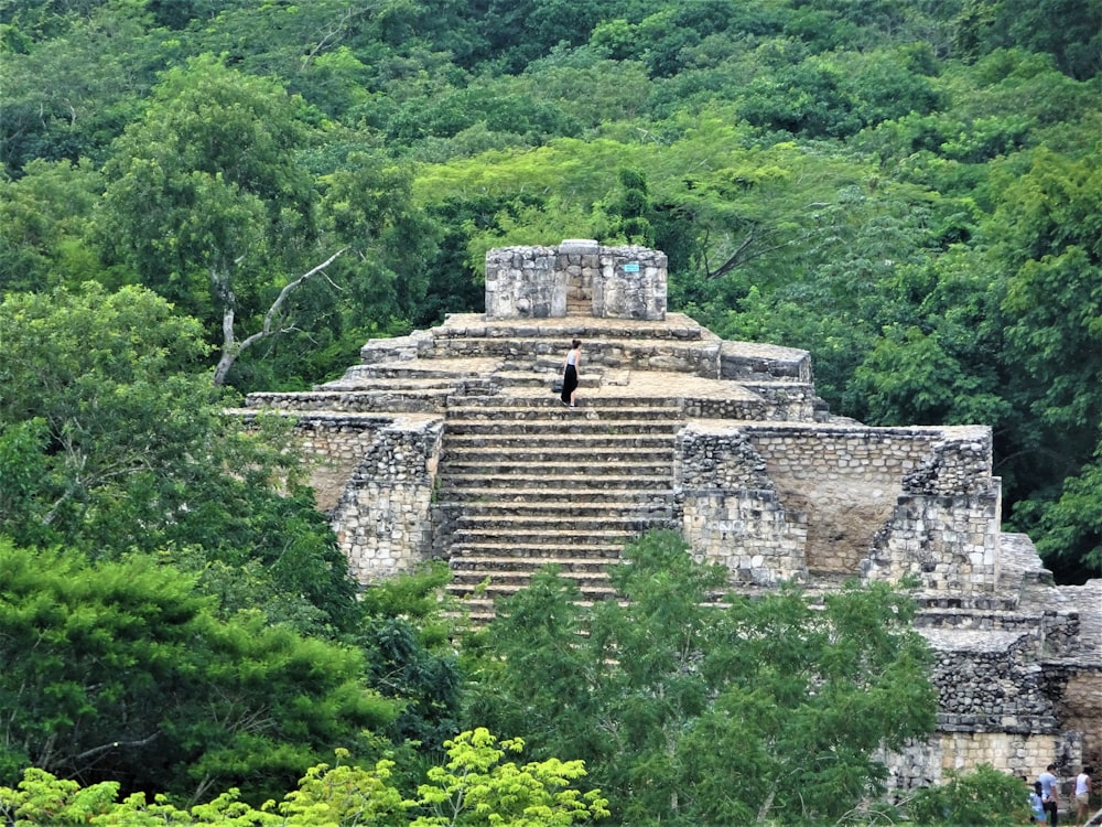 a person standing on a stone structure surrounded by trees