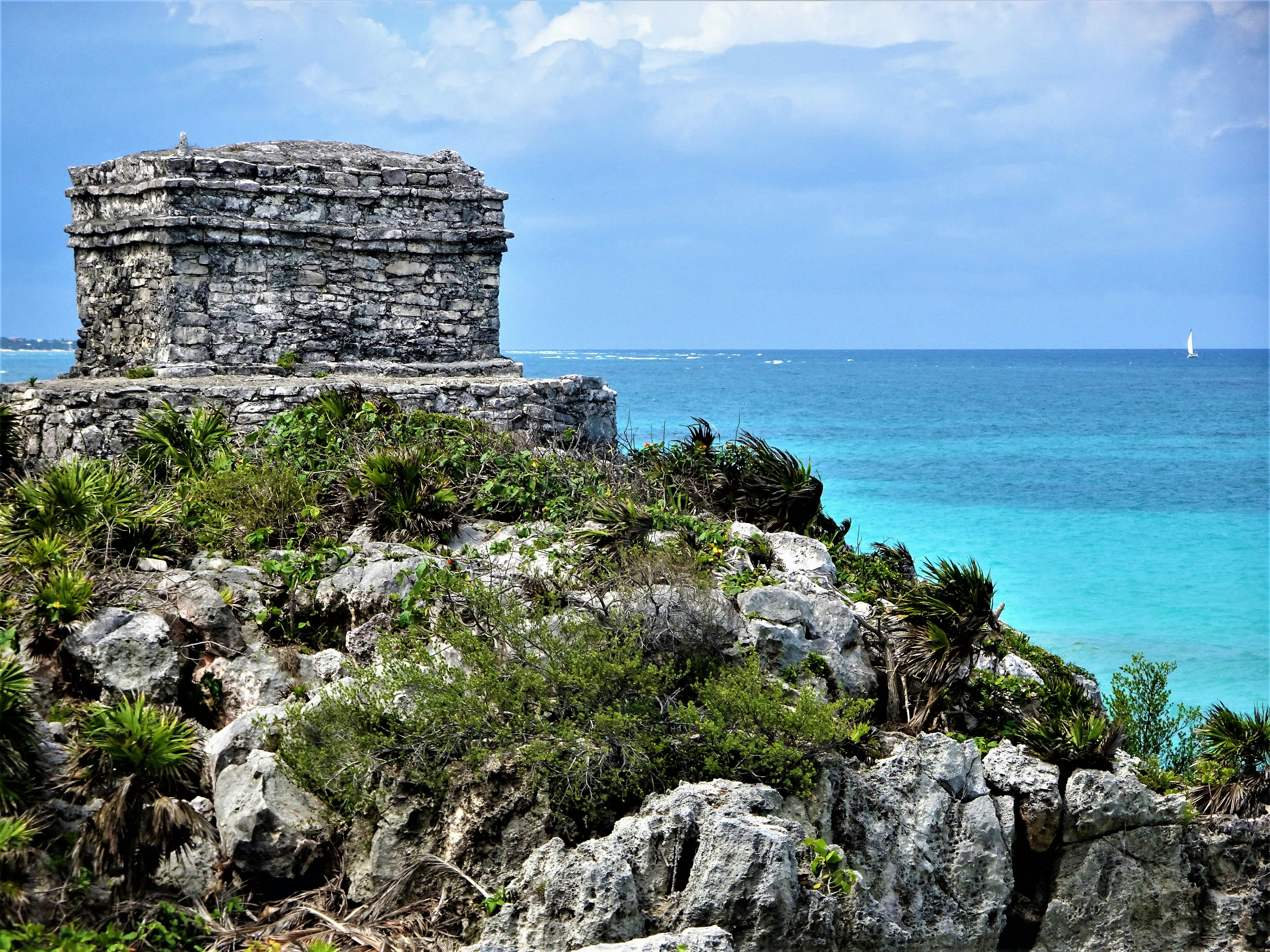 a stone structure on a rocky cliff overlooking the ocean with Tulum in the background