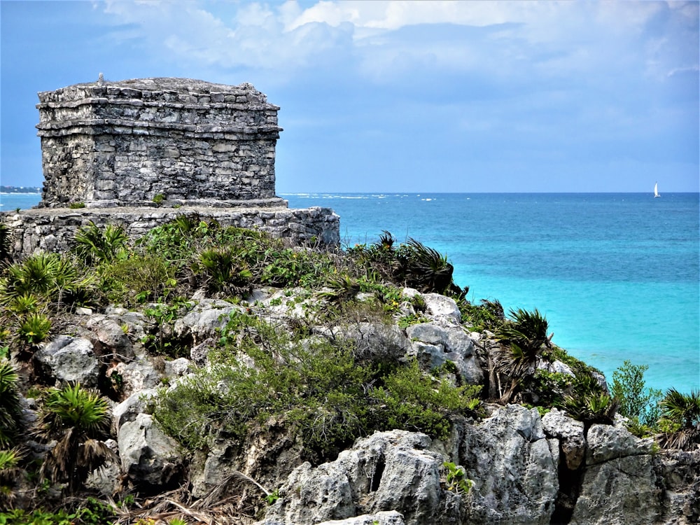 a stone structure on a rocky cliff overlooking the ocean with Tulum in the background