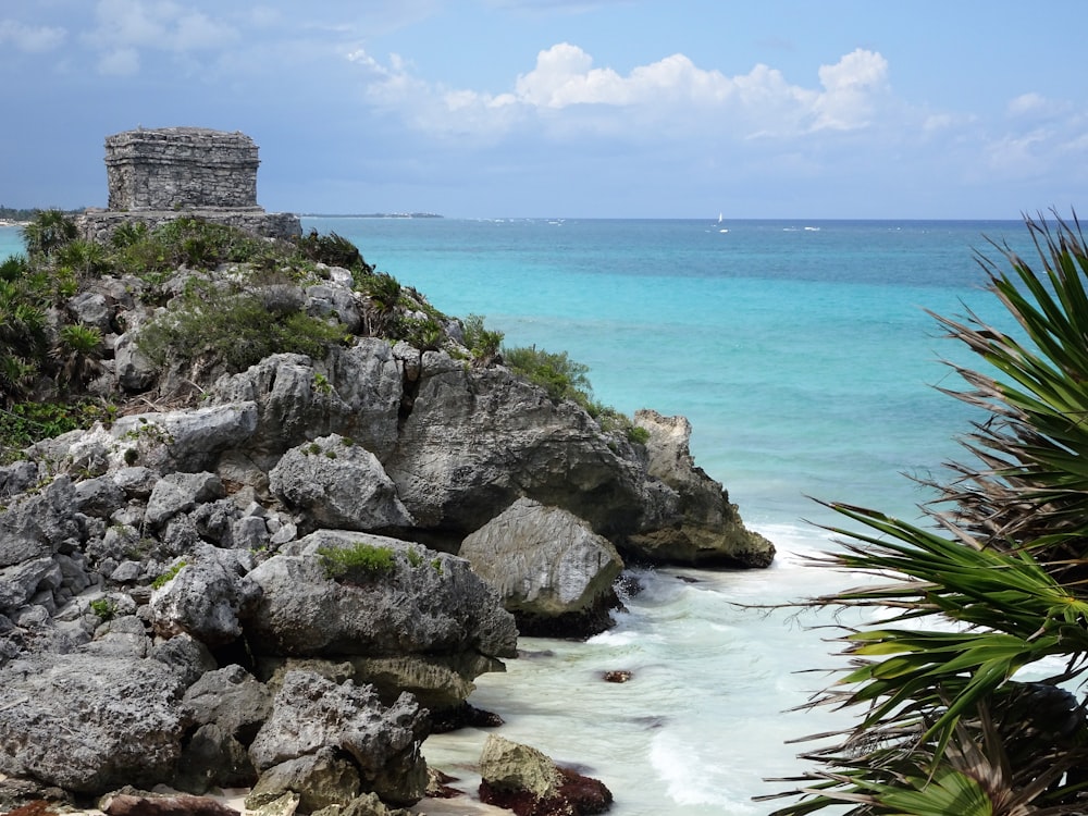 uma praia rochosa com um castelo em cima dela com Tulum ao fundo