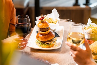 a person holding a glass of wine next to a burger and fries