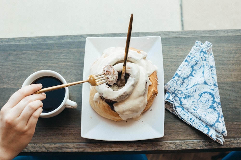 a hand holding a cup of coffee and a pastry with whipped cream