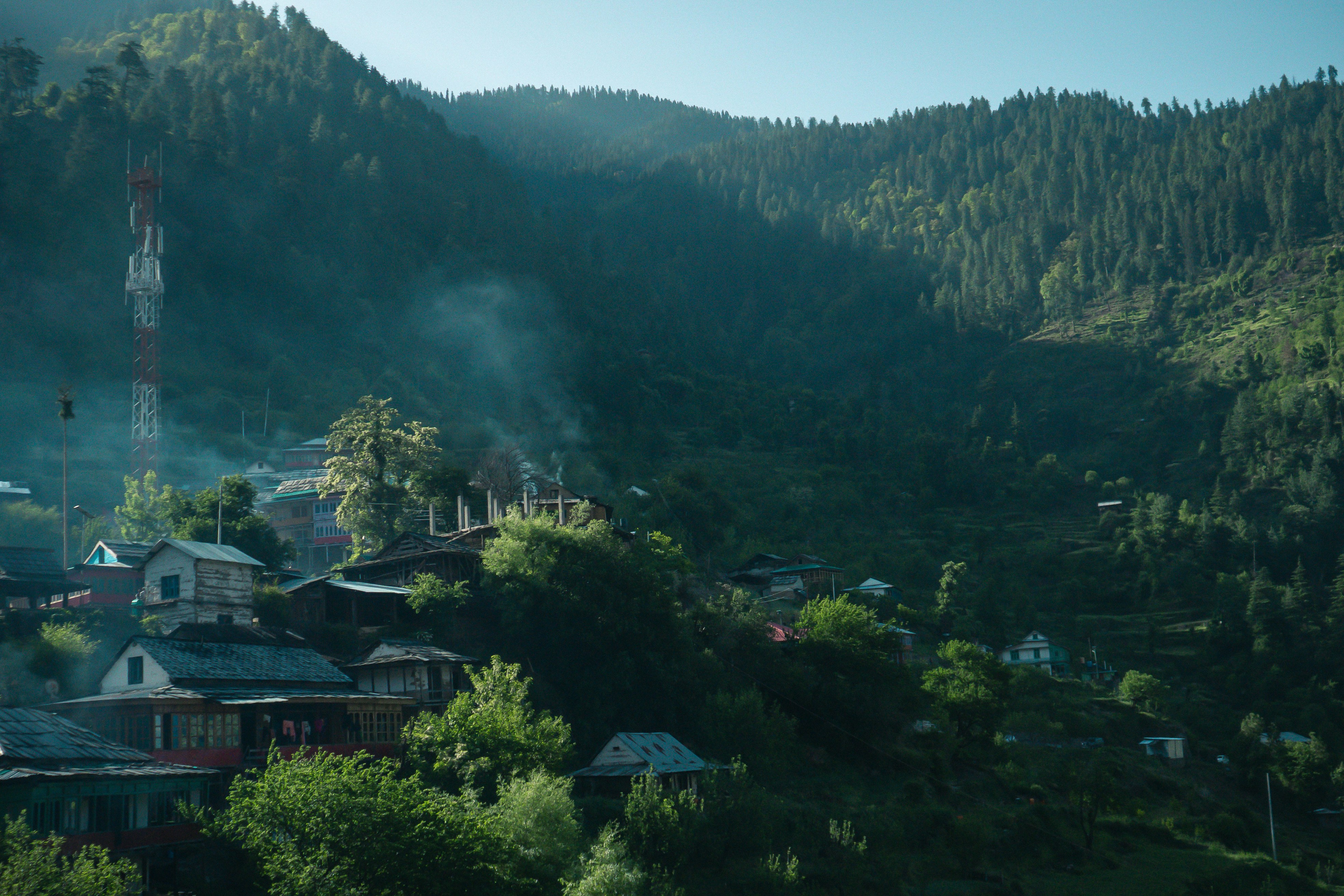 A panoramic view of a peaceful Kashmiri village nestled in a valley with mountains and lush greenery, depicting the aspiration for normal life.