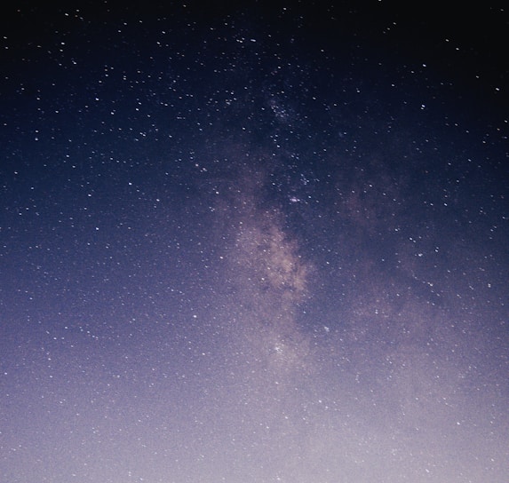 A star-filled night sky with the Milky Way galaxy prominently visible. The image captures numerous bright stars scattered across a dark, expansive sky. The galaxy's dense, light band adds a striking focal point.