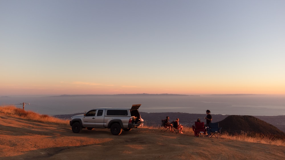 a group of people sitting on a road with a car and a sunset