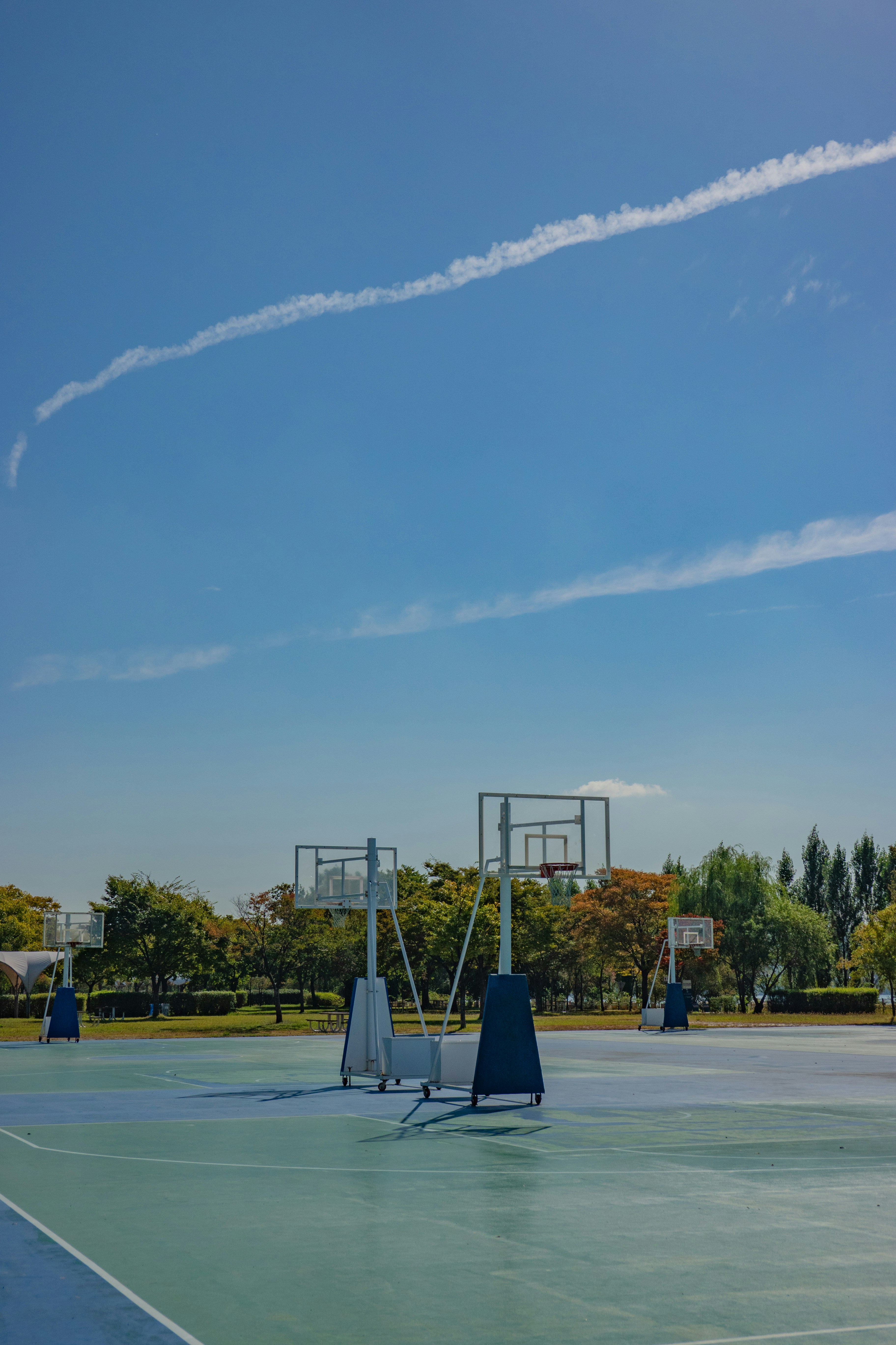 Outdoor basketball court with orange hoops, bright blue sky background, clean court lines