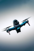 A close-up view of a quadcopter drone in flight with a streamlined design and prominent camera, set against a gradient blue sky background.