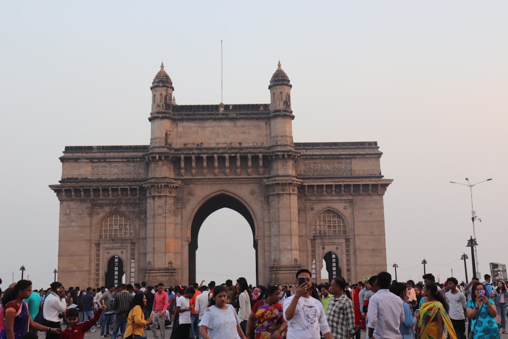 a large group of people walking in front of a large stone building with Gateway of India in the background