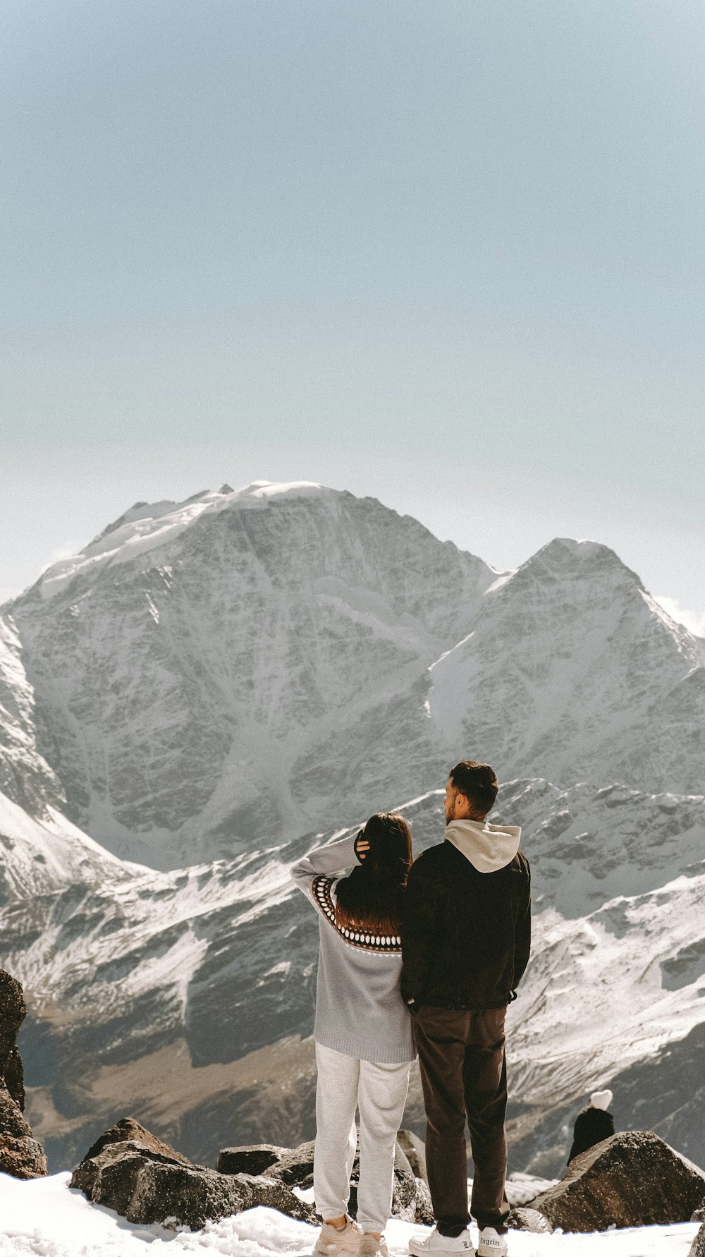 a man and woman standing on a mountain top with a mountain in the background