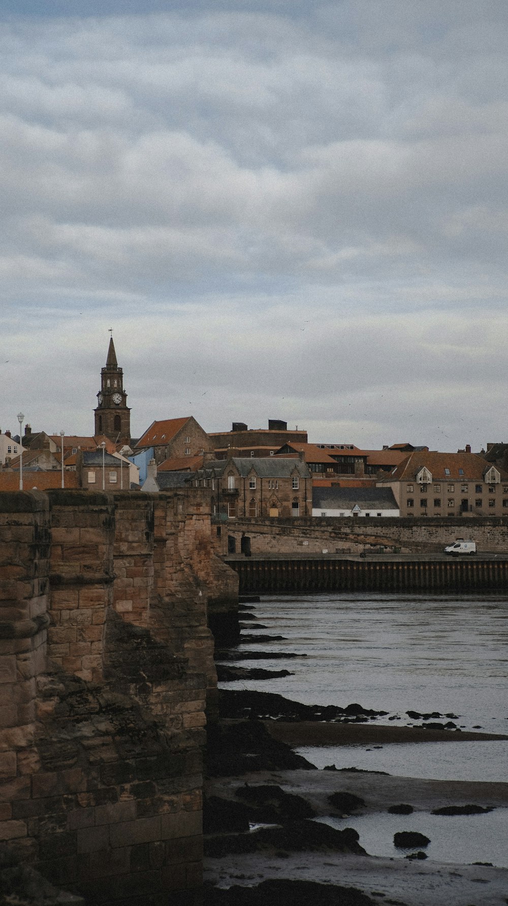 a stone wall with a clock tower and buildings by a body of water