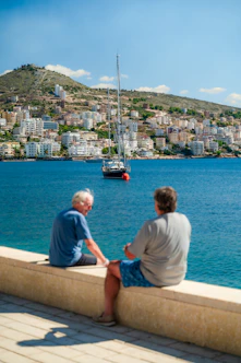 two men sitting on a ledge overlooking a city and a body of water