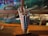 A collection of red and white striped paper straws is arranged in a clear glass on a wooden surface, with a glass of liquid on the left side. The background includes blurred reflections and a window, giving off colorful ambient lighting.