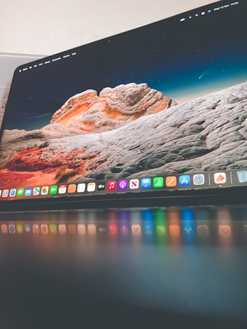 A sleek computer monitor displaying a colorful desktop background with a landscape of rocky formations under a starry sky. The foreground shows a glossy surface reflecting the vibrant colors of the desktop icons.