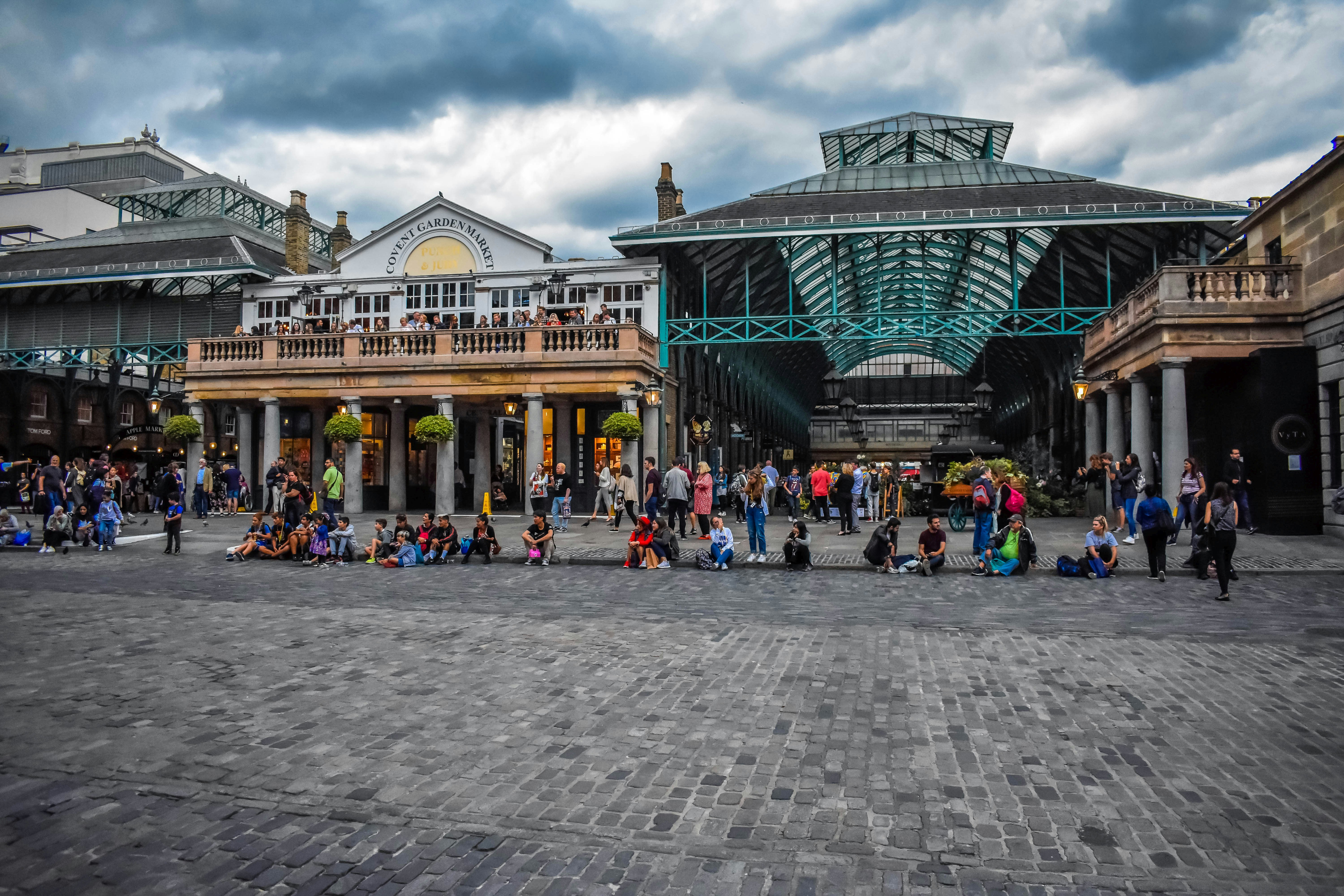 People gather in a public square near historic market buildings.