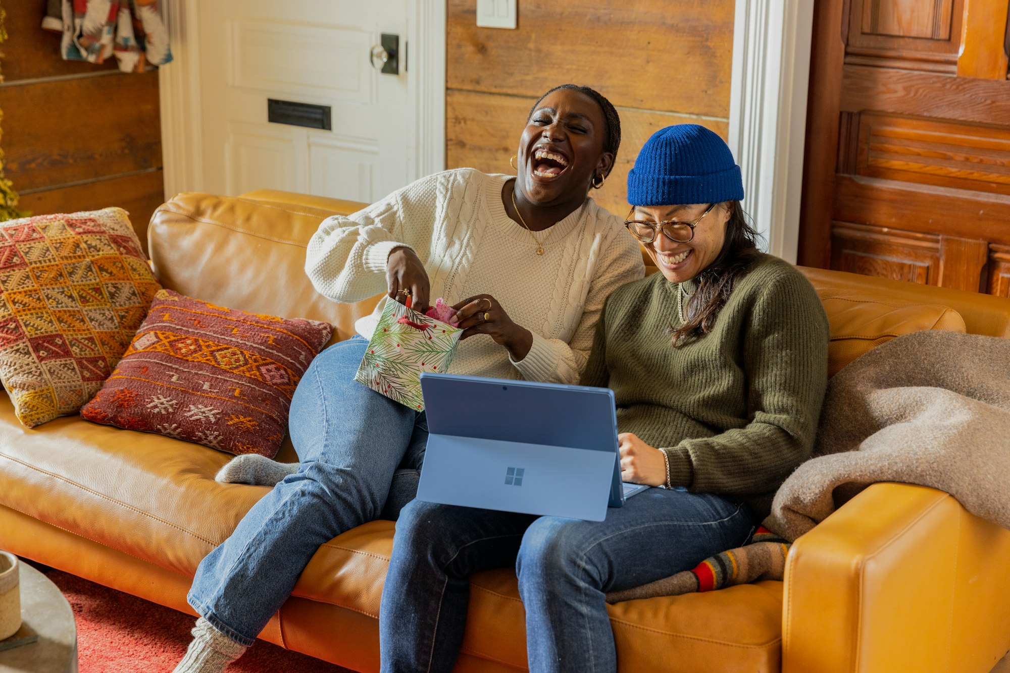 Deux femmes rigolant assise sur un canapé et regardant un ordinateur portable Microsoft