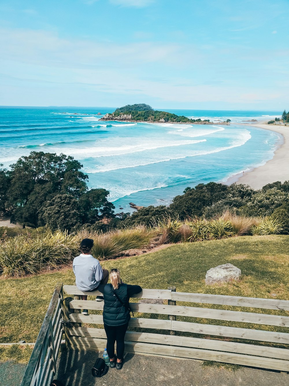 a man and woman standing on a wooden fence overlooking a beach